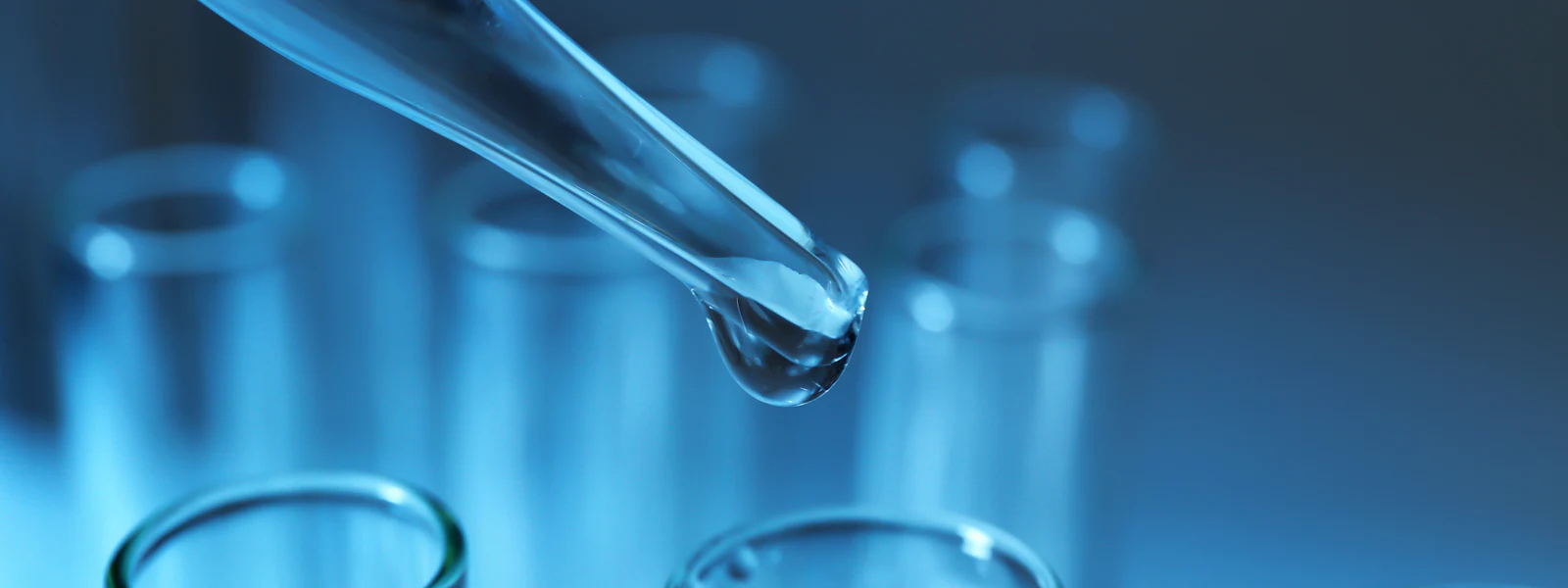 Pipette dripping sample into test tube A close-up image of a laboratory pipette dispensing a clear liquid into a row of transparent test tubes, set against a cool blue background, illustrating a scientific experiment or research setting.