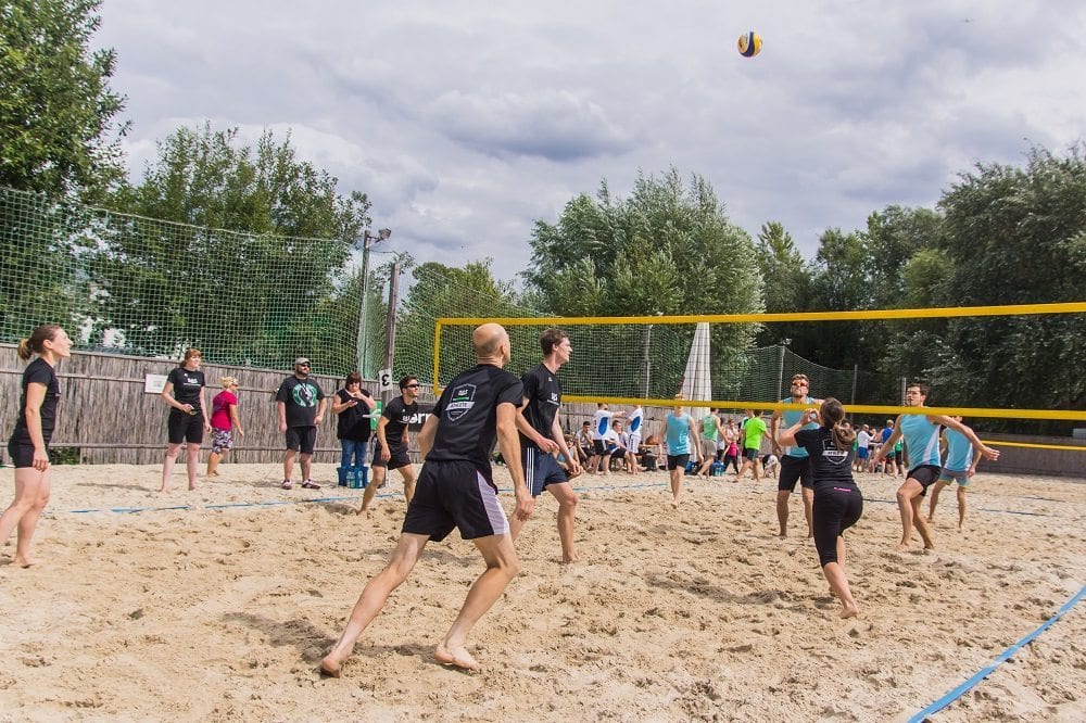 A group of people engaging in a lively beach volleyball game on a sandy court, surrounded by trees and a net, under a cloudy sky.