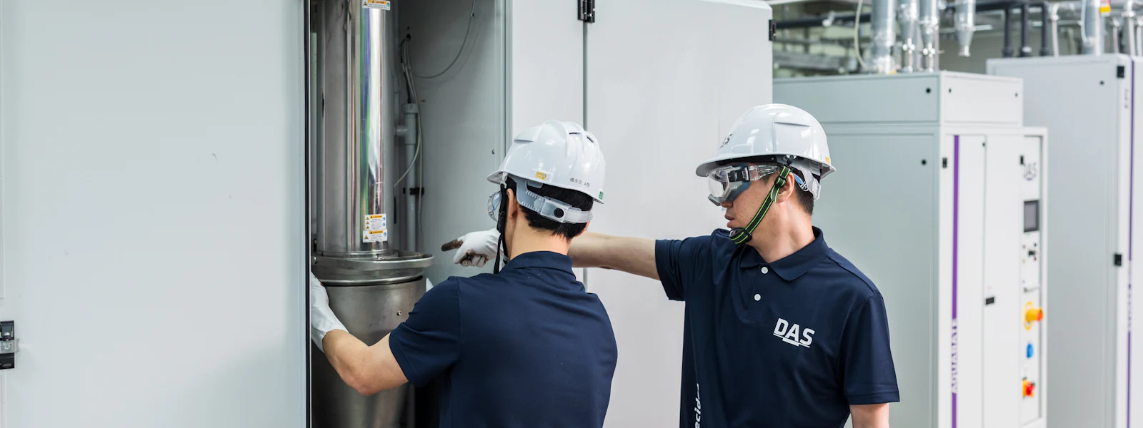 機台檢測 兩名身穿深藍色制服和安全帽的工人在工廠內操作大型機械設備,專注於維修和調整機器的細節。