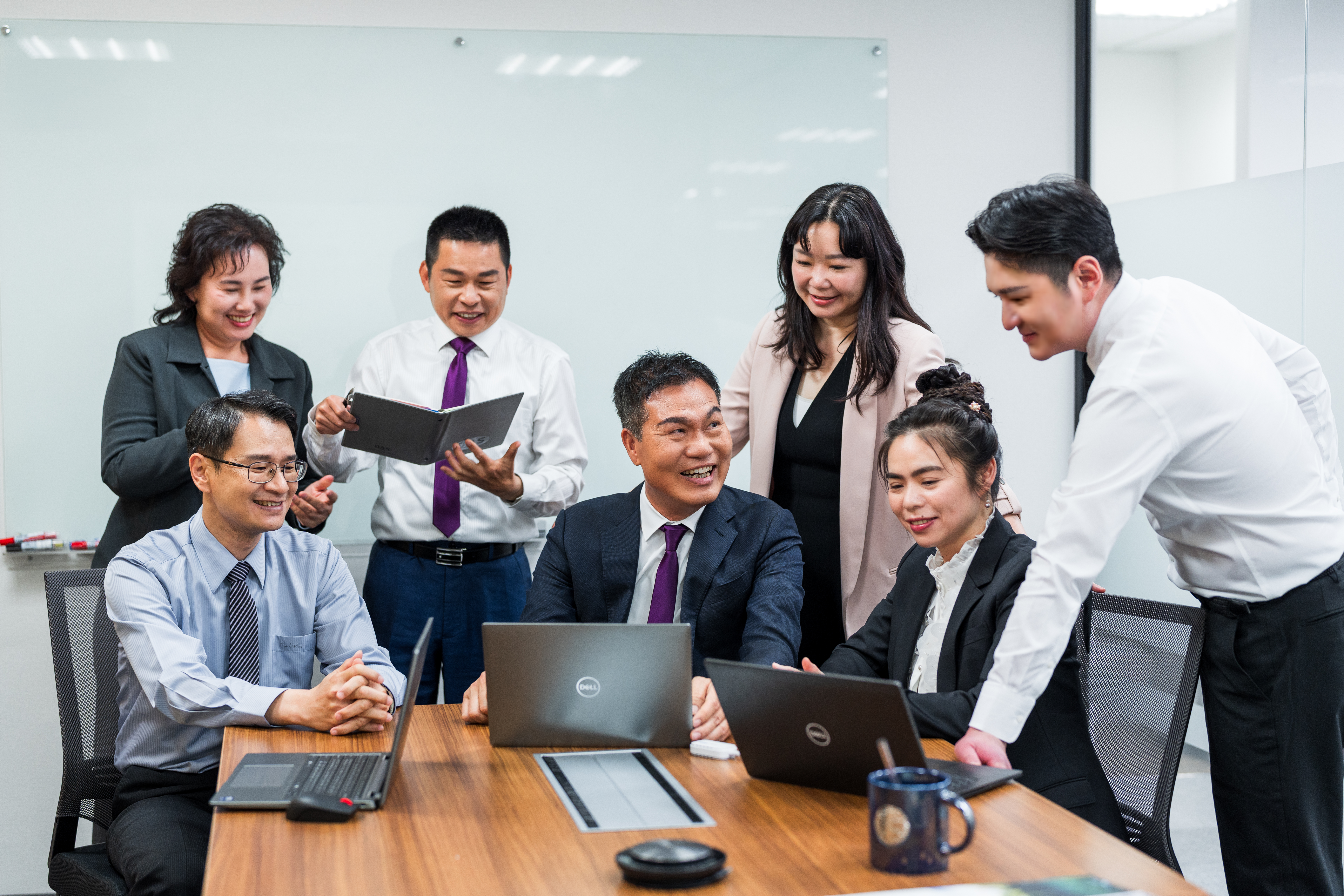 六位穿著正式服裝的商務人士在會議室內圍坐長桌，專注於筆記型電腦與文件，展現出協作和職場團隊精神。