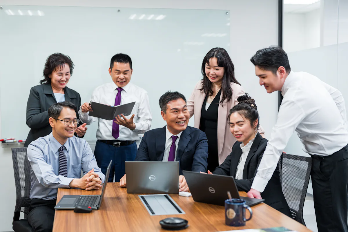 主管會議討論 六位穿著正式服裝的商務人士在會議室內圍坐長桌,專注於筆記型電腦與文件,展現出協作和職場團隊精神。