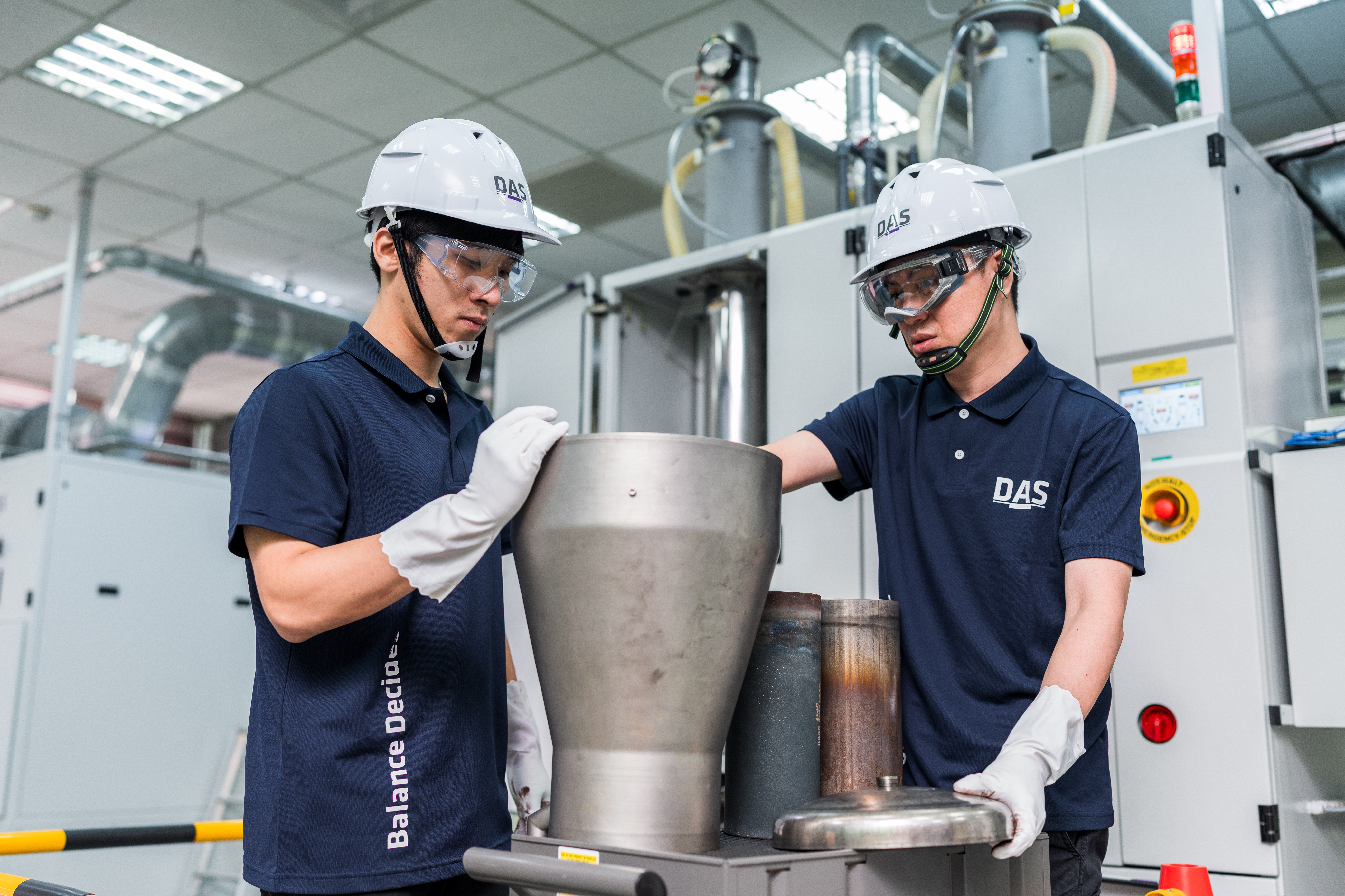 兩位穿戴安全設備的工人在工廠車間操作大型金屬容器背景。