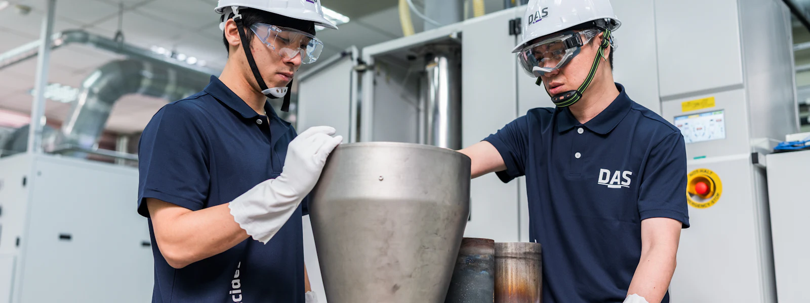 學習 兩位穿戴安全設備的工人在工廠車間操作大型金屬容器背景。