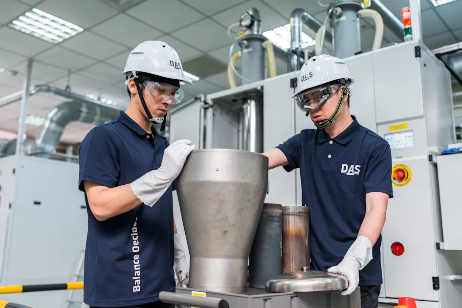 學習 兩位穿戴安全設備的工人在工廠車間操作大型金屬容器背景。