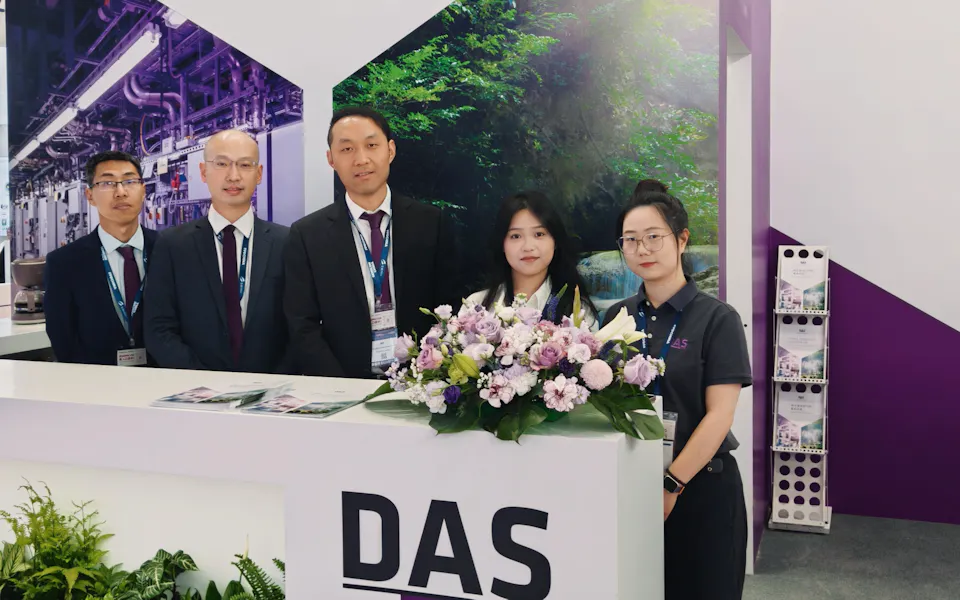 Impressions SEMICON China 2025 A group of five people, dressed in business attire, stand behind a booth with signage reading "DAS Environmental Experts," surrounded by vibrant greenery and a floral arrangement, suggesting a focus on green manufacturing innovations at a trade exhibition.