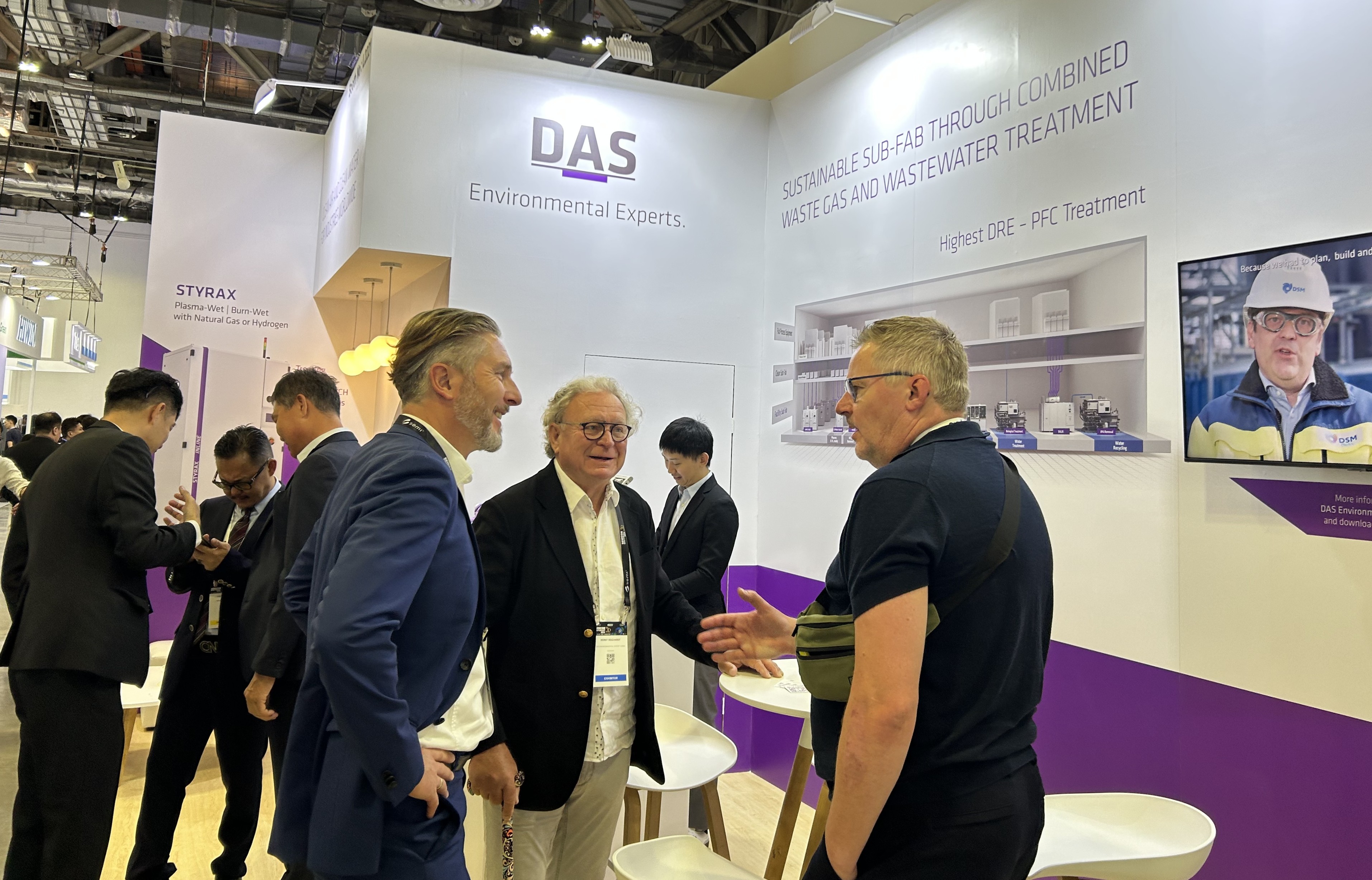 In a busy exhibition booth, several professionals engage in conversation under a sign that reads "DAS Environmental Experts," showcasing sustainable solutions for gas and wastewater treatment.