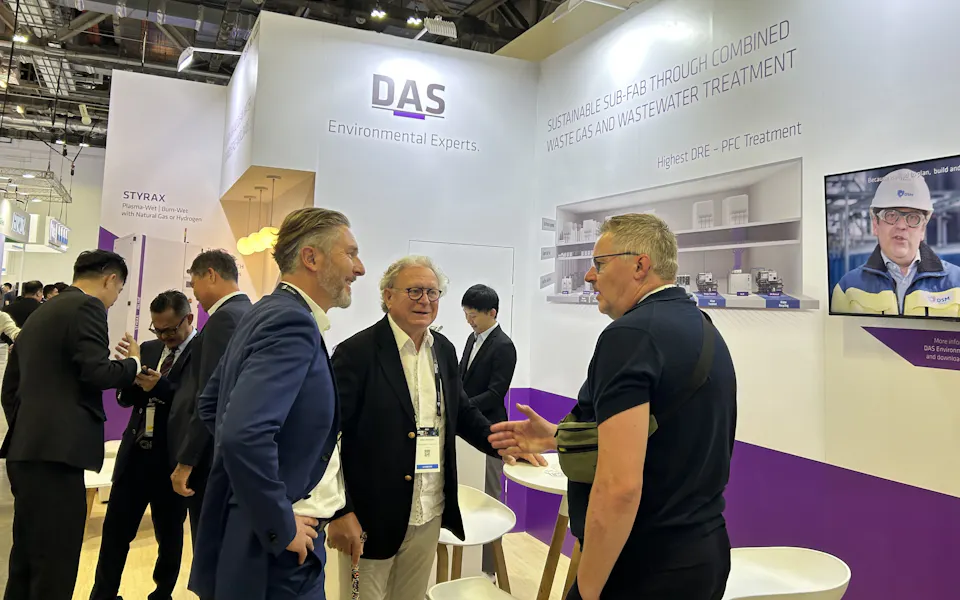 Impressions SEMICON SEA In a busy exhibition booth, several professionals engage in conversation under a sign that reads "DAS Environmental Experts," showcasing sustainable solutions for gas and wastewater treatment.