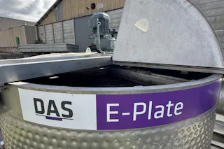 E-PLATE at Evers Specials B.V. A stainless-steel E-Plate system with a partially open lid is situated outdoors, with a background of industrial buildings and a clear blue sky.