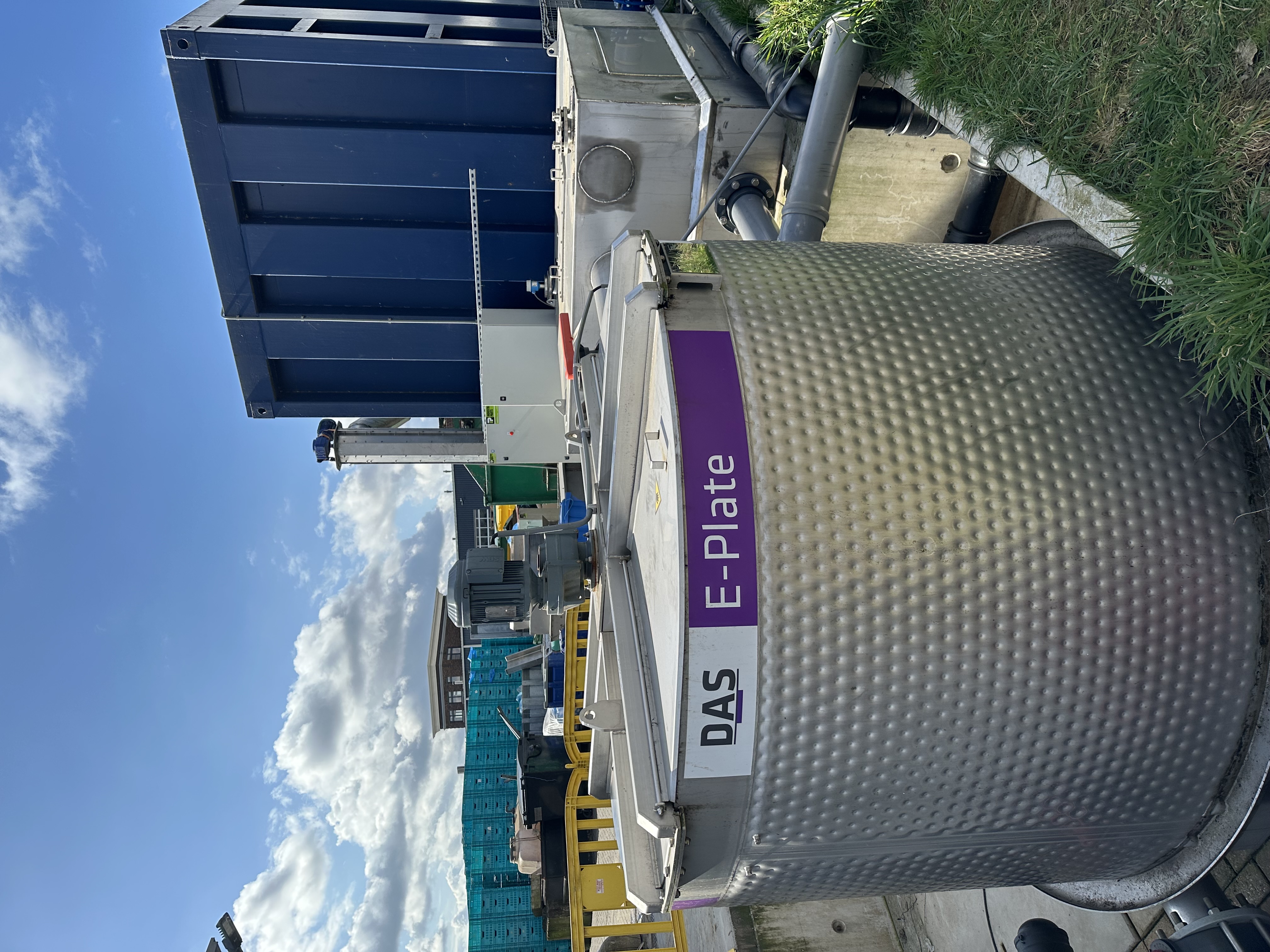 A large stainless steel container labeled "E-Plate" sits outdoors, partially shaded from the sun.
