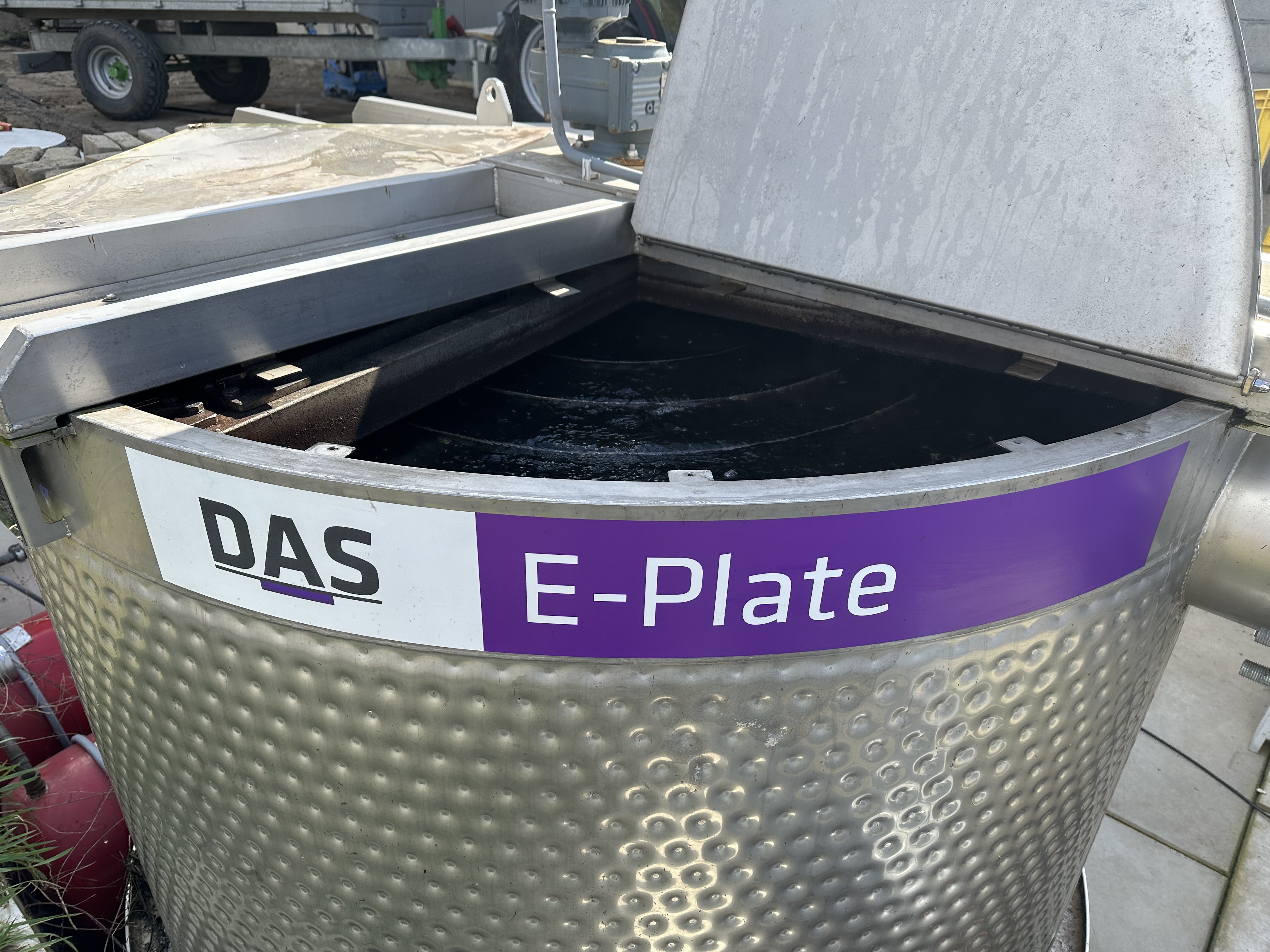 A stainless steel E-PLATE Heat Exchanger by DAS EE with a partially opened lid, featuring a textured surface and prominent branding labels, positioned in an industrial outdoor setting.