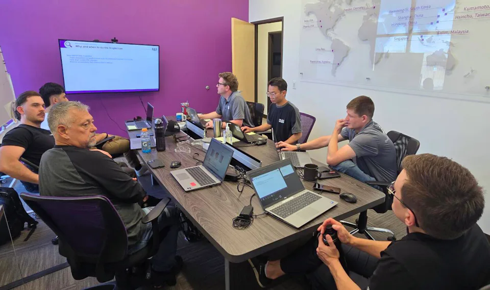 ISC Opening - 2 A group of people in a modern conference room engage in a meeting with laptops on a large table, a screen displaying a presentation on a purple wall, and a world map on an adjacent wall, capturing a collaborative work environment.