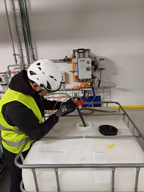 Chemical physical water treatment for sc customer A worker in a safety vest and helmet examines a large liquid storage container with a control panel and pipes in the background, emphasizing industrial safety procedures.