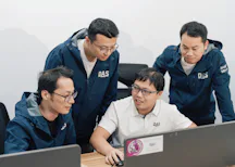 Service teams worldwide four male employees from asia with blue jackets and white shorts in front of laptops