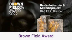 Brownfield Award 2022 DAS EE 이미지에는 "Brown Field Award 2022" 로고와 함께 "Bestes Industrie- & Gewerbeprojekt"라는 문구가 있으며, 배경에는 두 개의 자연석이 놓여 있습니다.