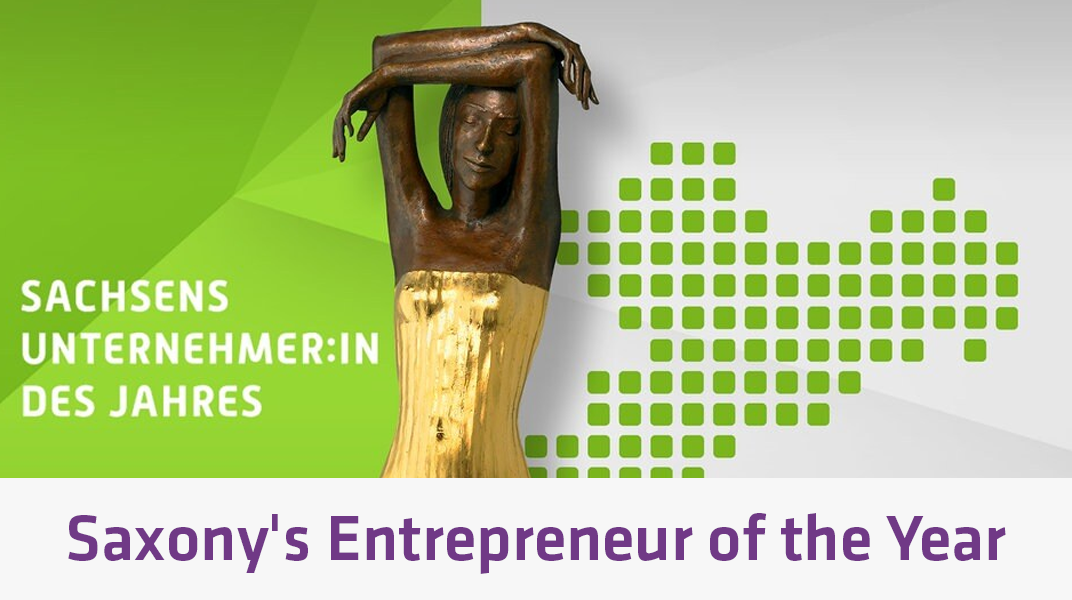 이 이미지에는 양팔을 머리 위로 들어 올린 인물의 청동상이 담겨 있으며, 녹색 그라데이션과 픽셀 처리된 작센 주 지도가 배경으로 깔려 있고, “Sachsens Unternehmer:in des Jahres”라는 문구가 함께 적혀 있어 ‘작센 주 올해의 기업가’ 상을 상징하고 있습니다.