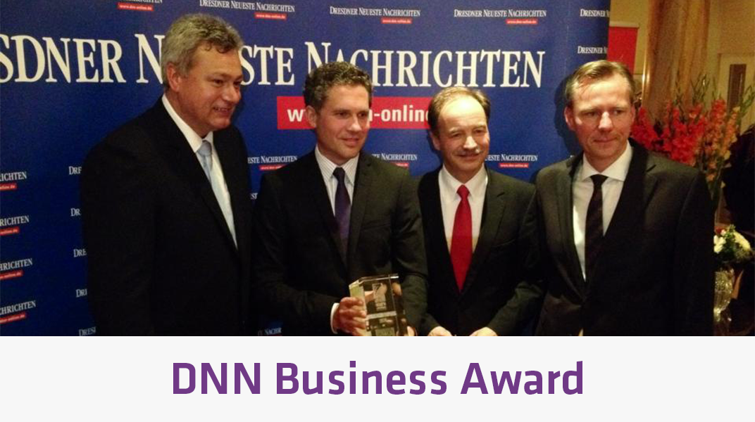 사람들이 정장 차림으로 DNN 비즈니스 어워드 행사에서 포토월 앞에서 상을 들고 포즈를 취하고 있습니다.