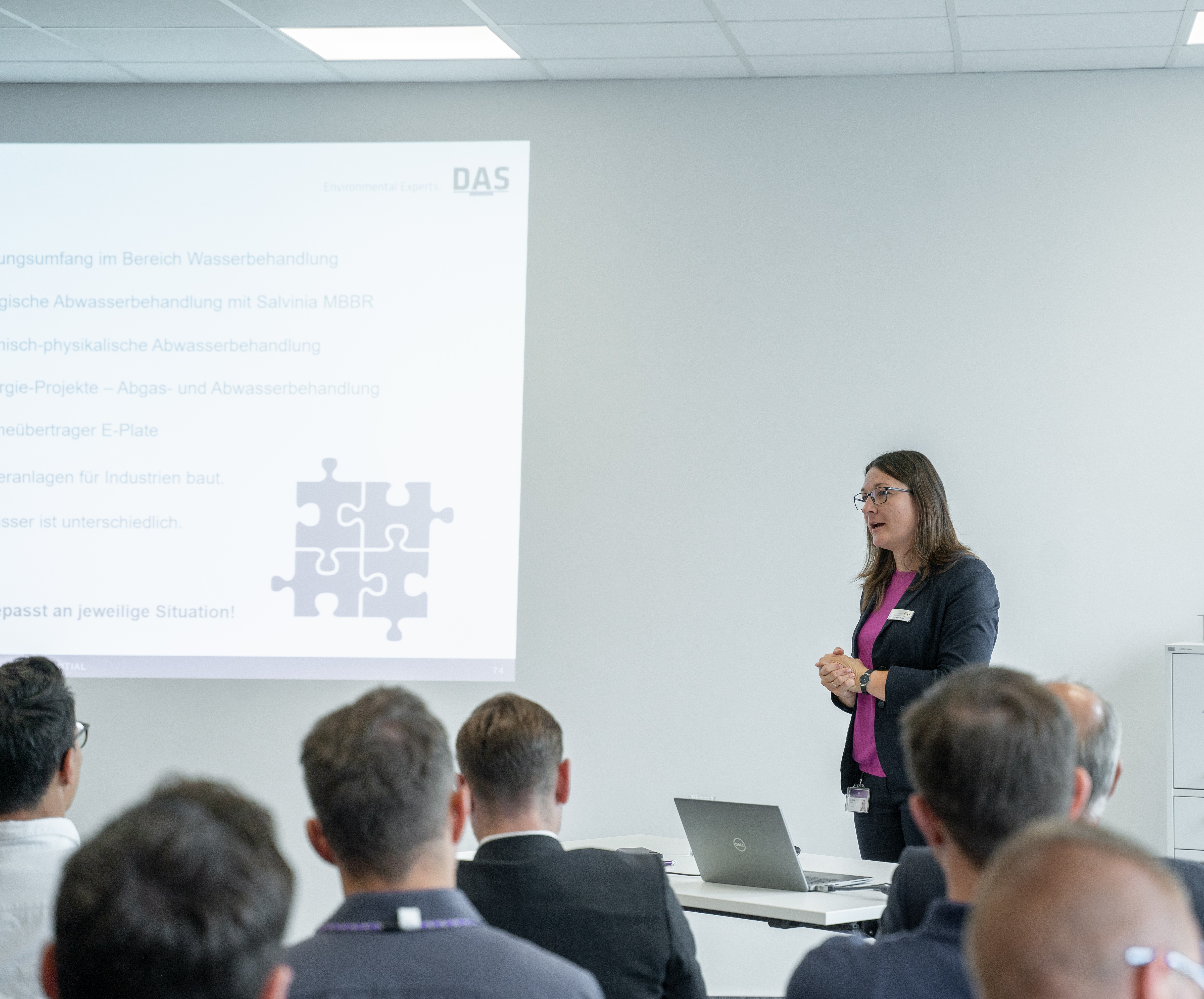 Business professionals attend a presentation in a modern conference room, where one person stands at a podium while another operates a projector displaying slides about strategic planning.
