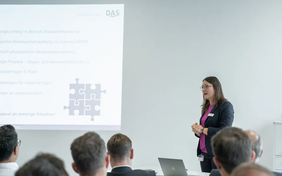 Visual Gate Business professionals attend a presentation in a modern conference room, where one person stands at a podium while another operates a projector displaying slides about strategic planning.