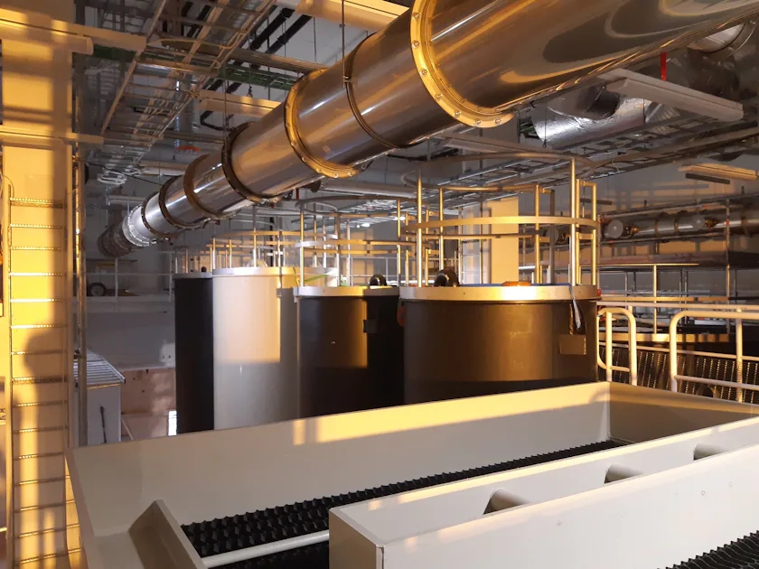 DAS system for chemical and physical water treatment A large industrial interior, featuring huge metal tanks and a complex network of pipes, is bathed in warm, natural sunlight.