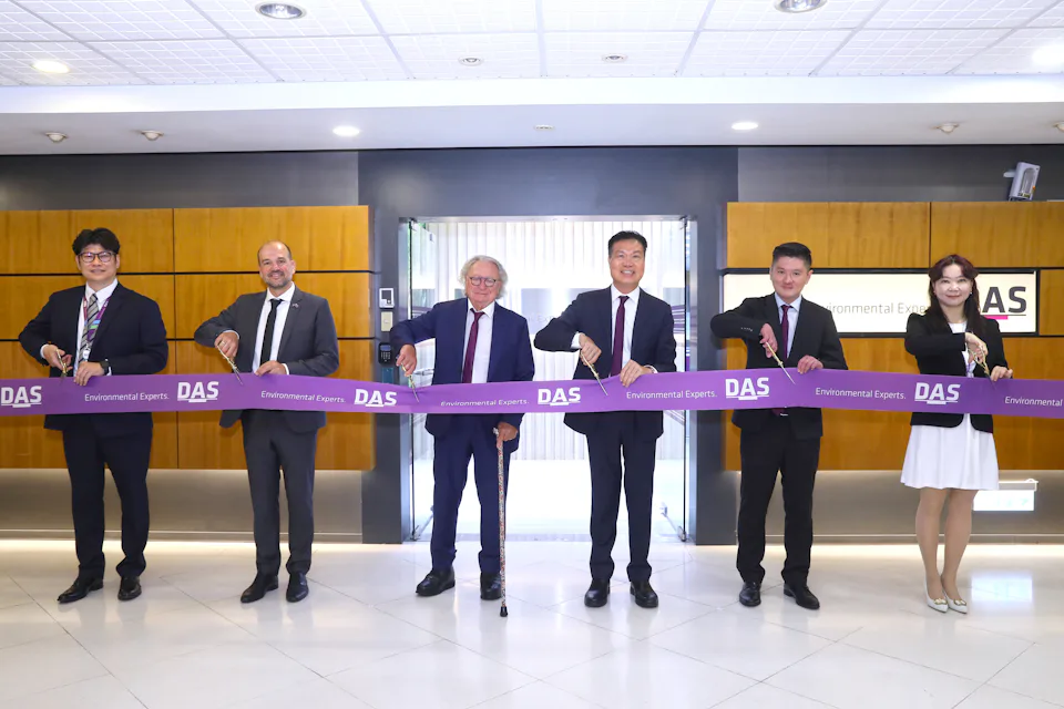 DAS TW HC office opening 在辦公室大廳內,六位穿著正式服裝的人員站在一起,手持印有"DAS Environmental Experts"字樣的紫色剪綵帶,背景是木製牆面和透明玻璃門。