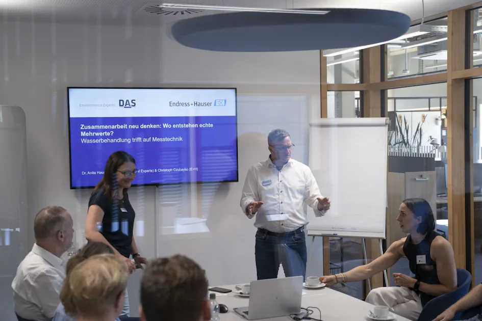 Roundtables 2026 Eine Gruppe von Menschen sitzt in einem modernen Konferenzraum mit Glaswänden; auf einem großen Bildschirm sind Präsentationsfolien zur Wasserbehandlung und Messtechnik zu sehen, während ein Mann am Whiteboard steht und diskutiert.
