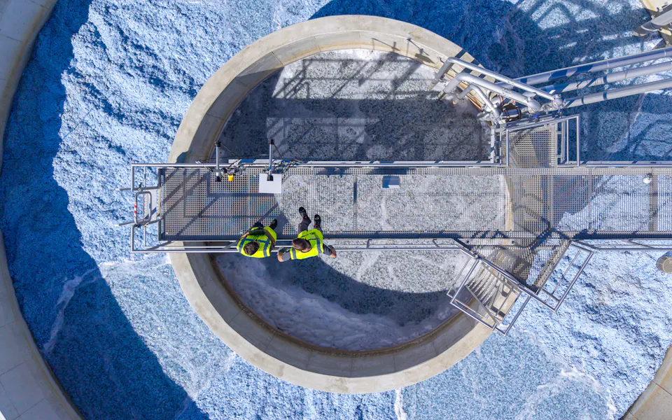 Emsland Aller Aqua Plant Aerial view of two engineers in high-visibility clothing inspecting a circular wastewater treatment facility with foamy water, highlighting industrial water management and environmental engineering.