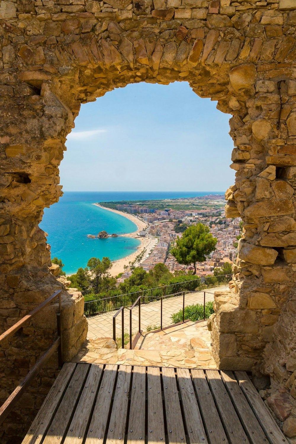 Panoramic view of Blanes Beach through a stone gate of San Juan Castle