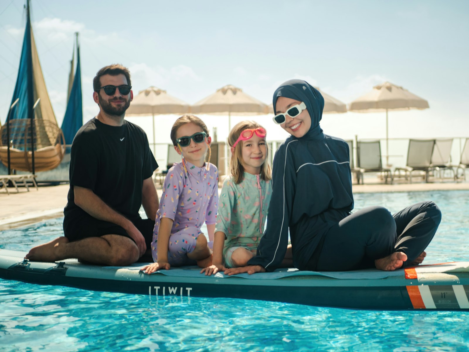 A family on a paddle board in a resort pool with sail canopies behind, from a Halalbooking photoshoot in Antalya