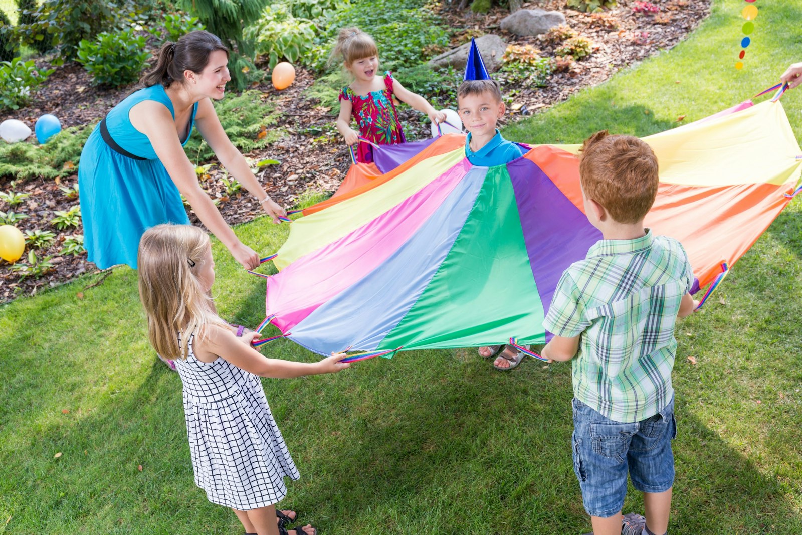 A kids’ club animator playing a parachute game with children on a lawn