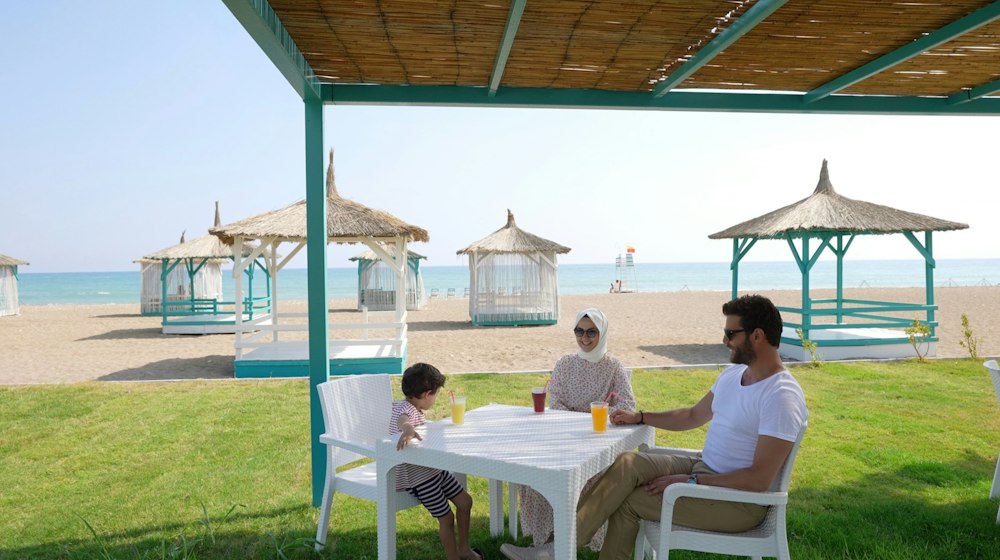 A family at a shaded table on the lawn by the beach at Rizom Beach Hotel Kumluca