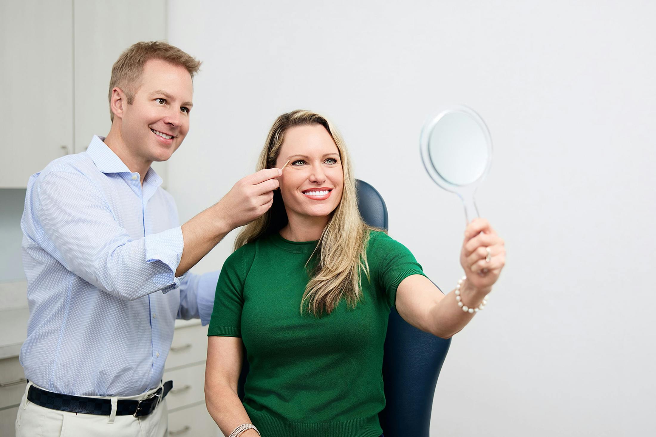 patient holding up handheld mirror with doctor looking at her eyes