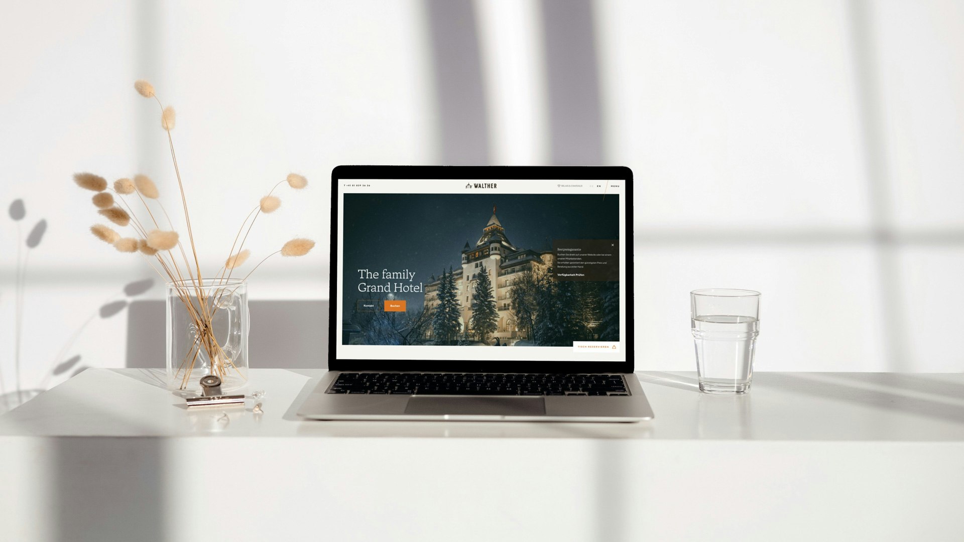 Laptop on white table displaying Hotel Walther website with a winter hotel facade.