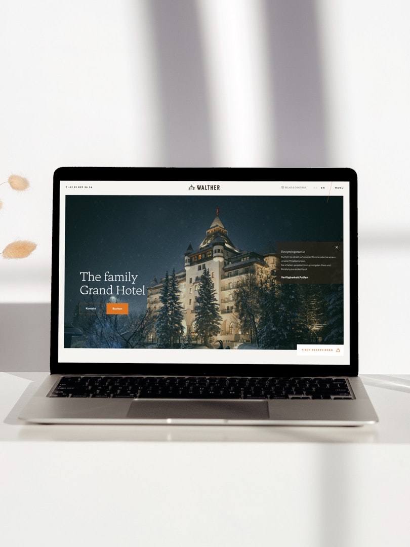 Laptop on white table displaying Hotel Walther website with a winter hotel facade.