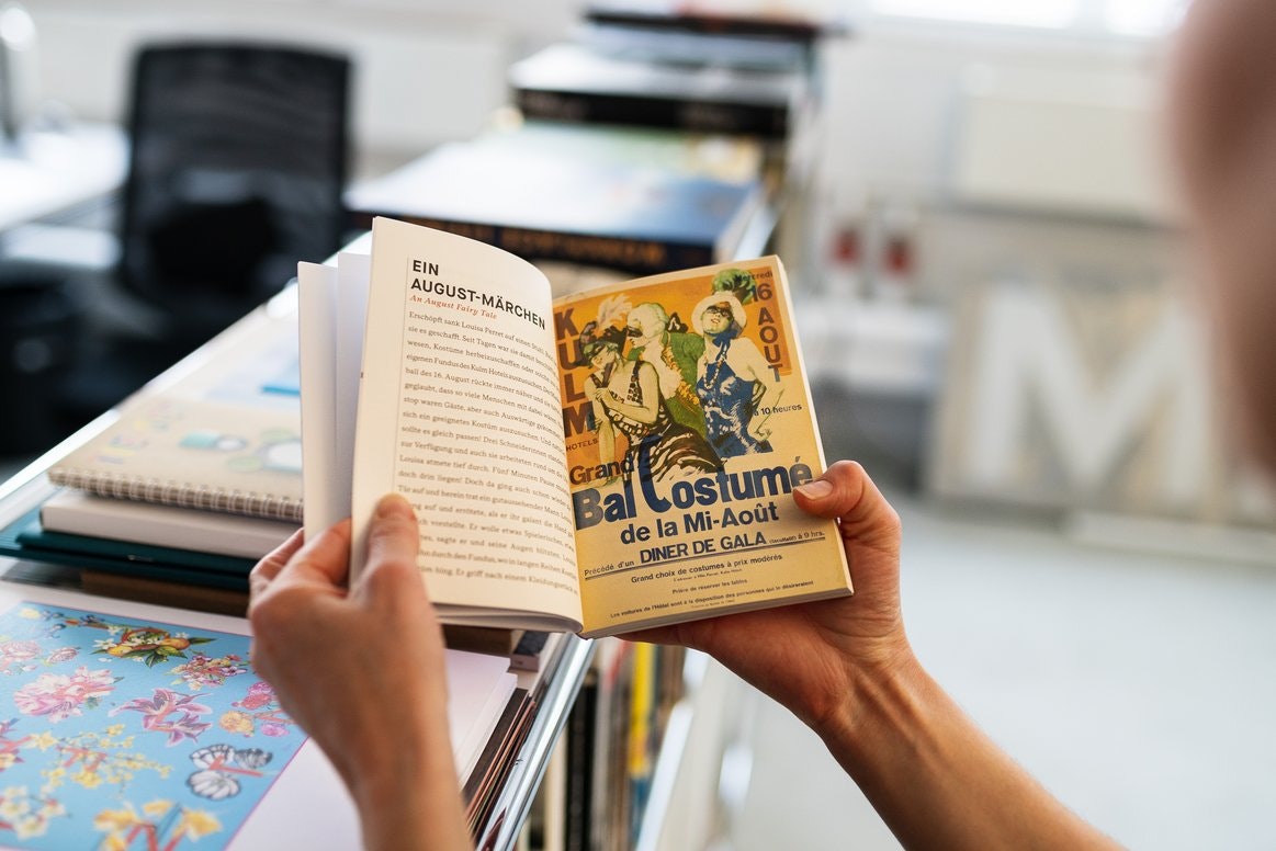 Aufgeschlagenes Buch mit Kapitel „Ein August-Märchen“ und Plakatillustration.