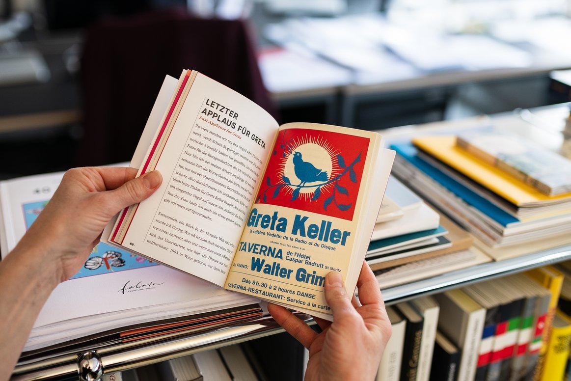 Aufgeschlagenes Buch mit Kapitel „Letzter Applaus für Greta“ und Vintage-Plakat.