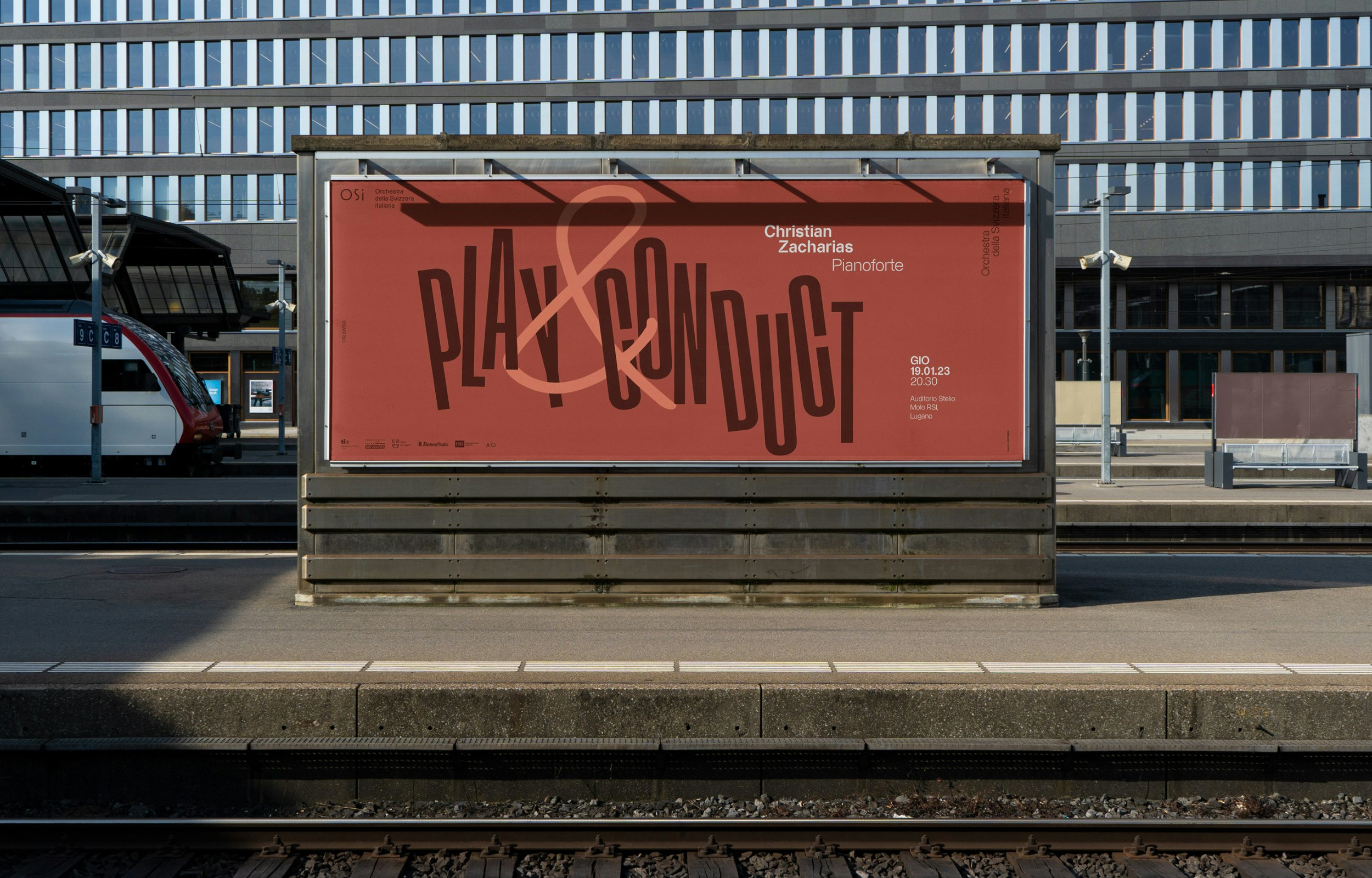 Red poster at the train station with the text “Play & Conduct” and concert details of Orchestra della Svizzera italiana.
