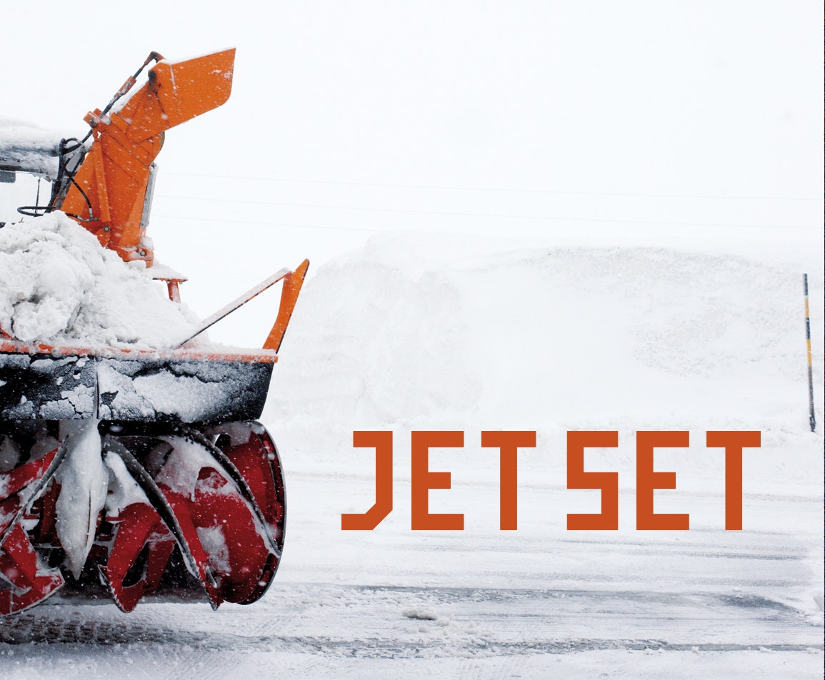 Snow blower with red auger ejecting snow, next to the text “JET SET” in orange letters on a white winter background.