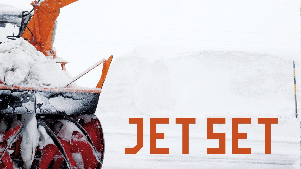 Snow blower with red auger ejecting snow, next to the text “JET SET” in orange letters on a white winter background.