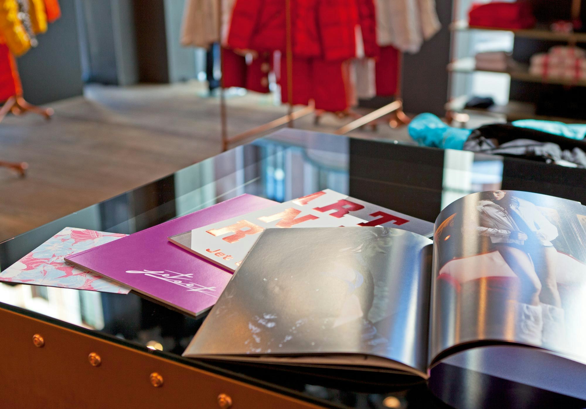 Aufgeschlagene Jet-Set-Lookbooks und Kataloge auf einem Tisch im Store, mit Modefotos und glänzendem Druck.