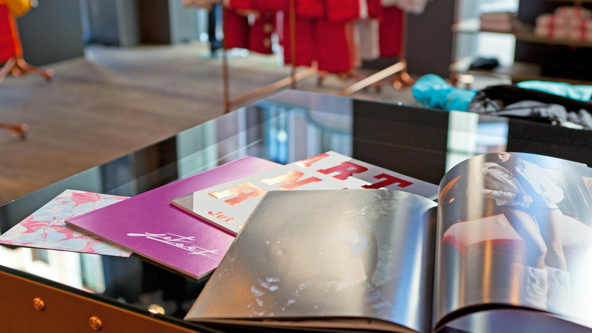 Aufgeschlagene Jet-Set-Lookbooks und Kataloge auf einem Tisch im Store, mit Modefotos und glänzendem Druck.