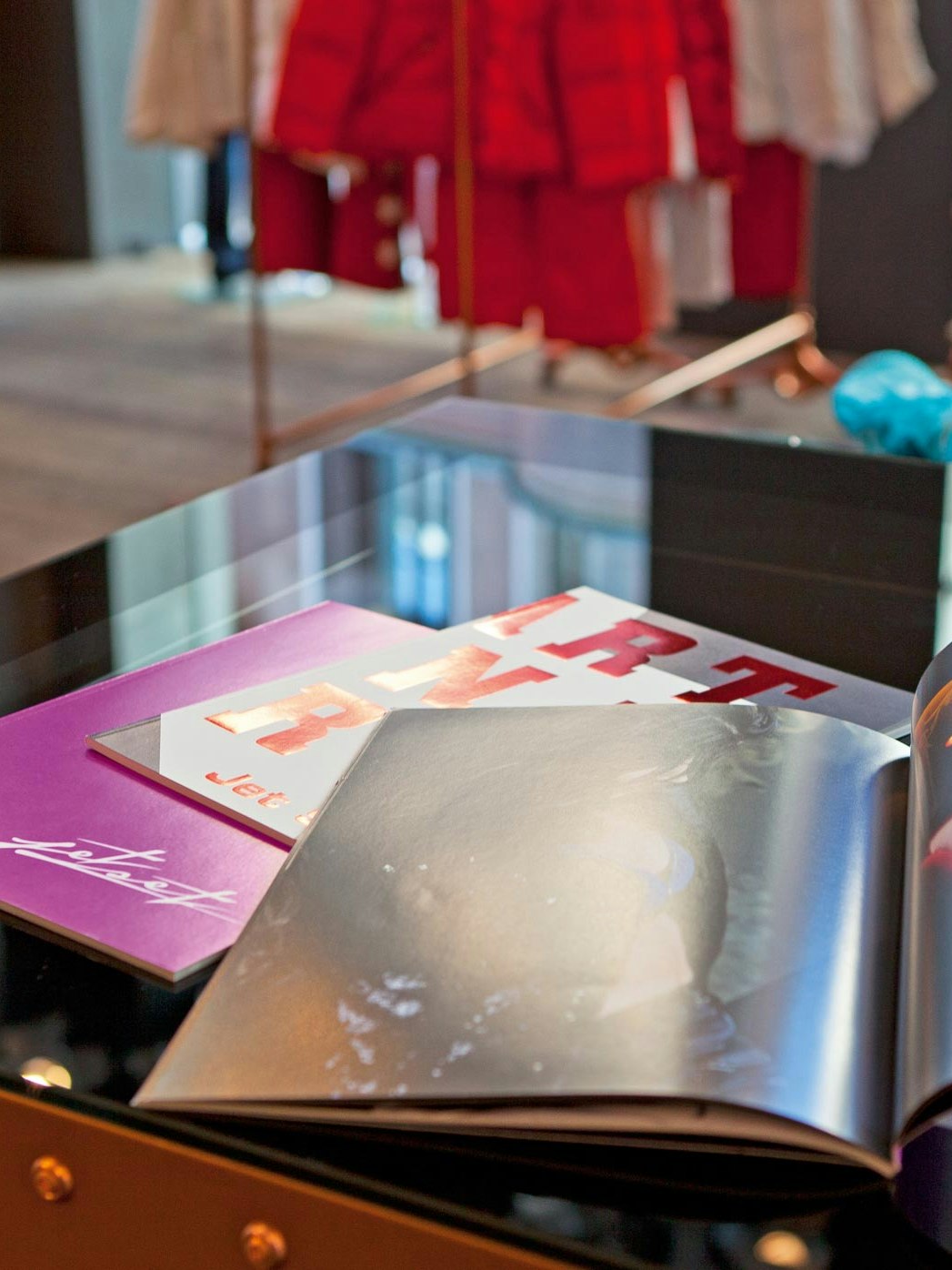 Aufgeschlagene Jet-Set-Lookbooks und Kataloge auf einem Tisch im Store, mit Modefotos und glänzendem Druck.