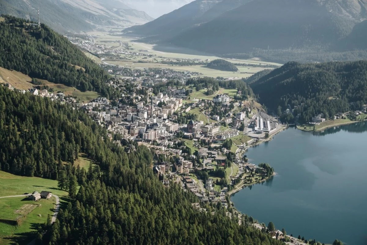 Aerial view of St. Moritz and the Upper Engadine, with the lake on the right and surrounding mountains in the background.