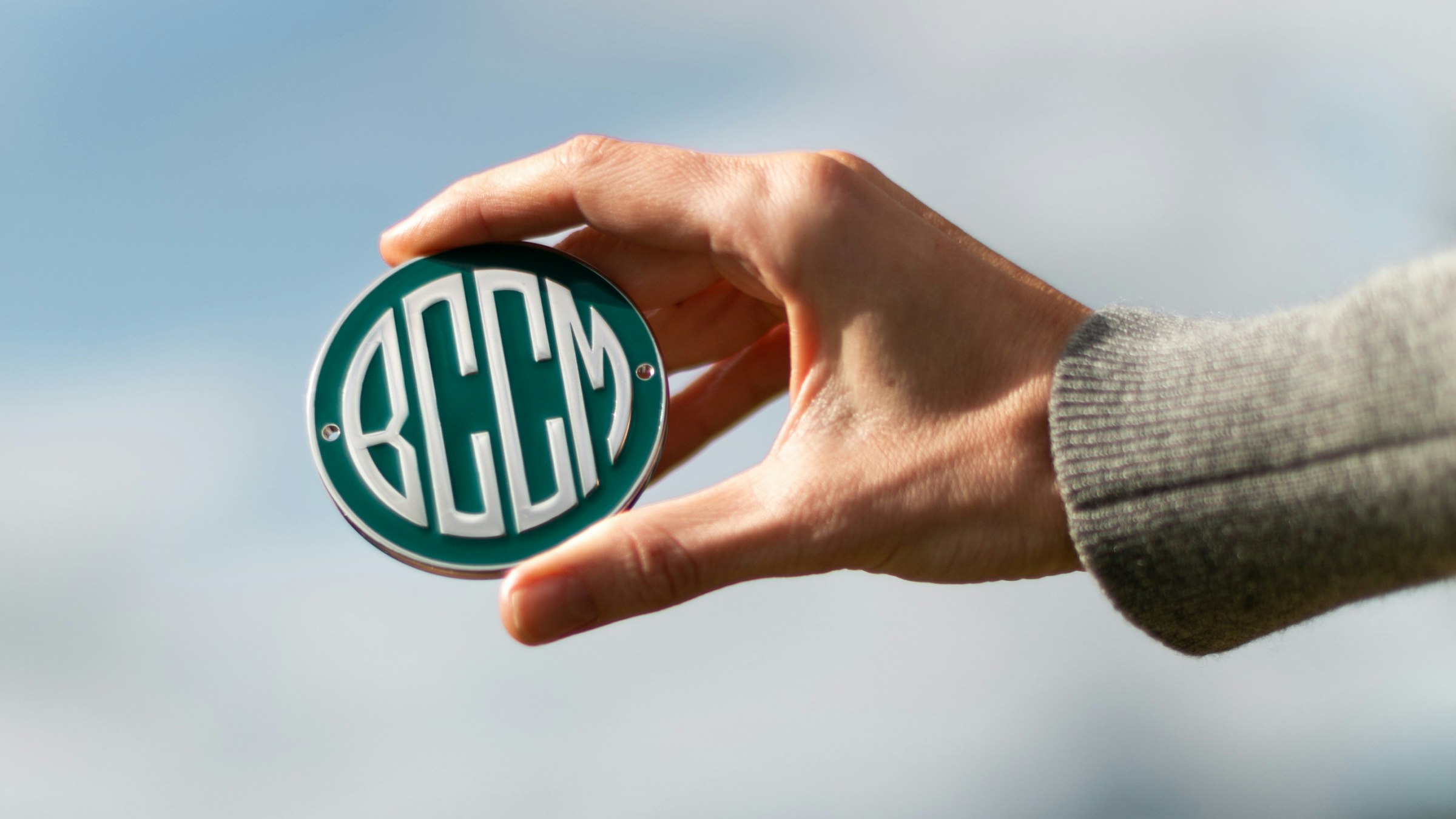 Hand mit rundem BCCM-Logo-Emblem vor blauem Himmel