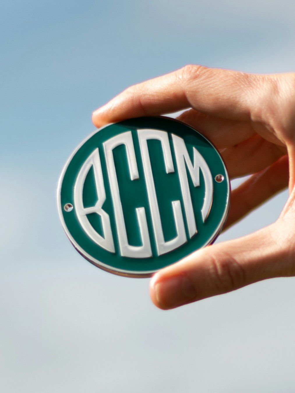 Hand mit rundem BCCM-Logo-Emblem vor blauem Himmel