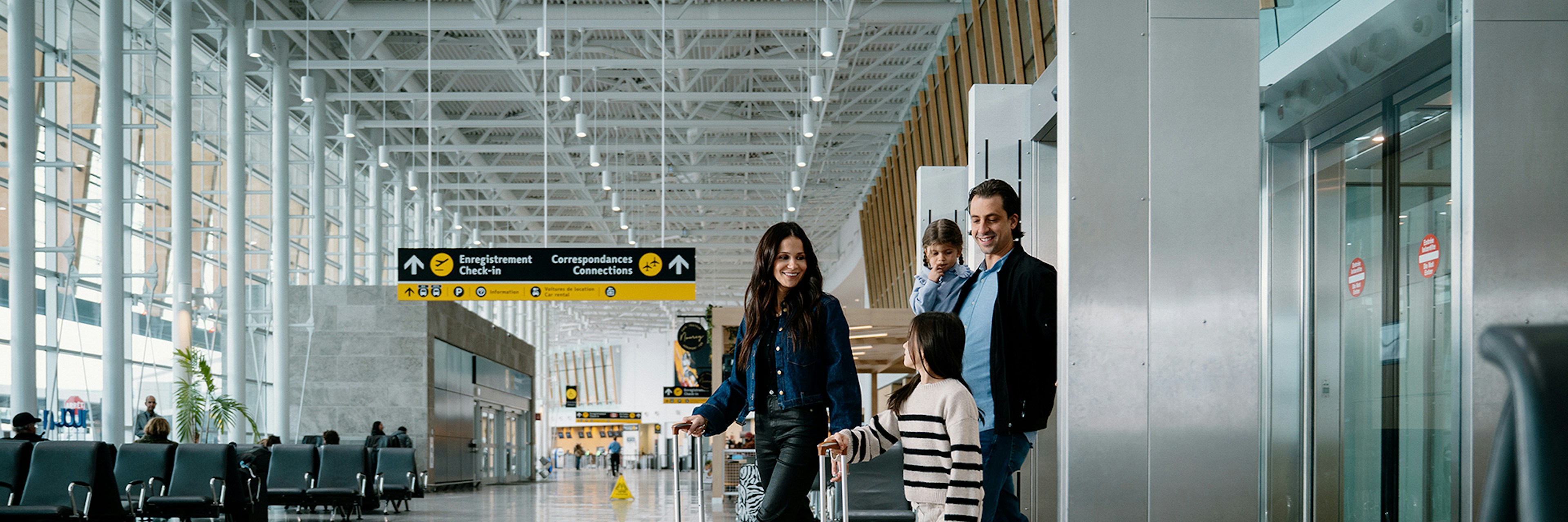 Une famille de quatre personnes, accompagnée de ses bagages, traverse un terminal d'aéroport spacieux et moderne. On aperçoit des panneaux indicateurs et des coins où s'asseoir ; la famille semble heureuse et prête à partir.