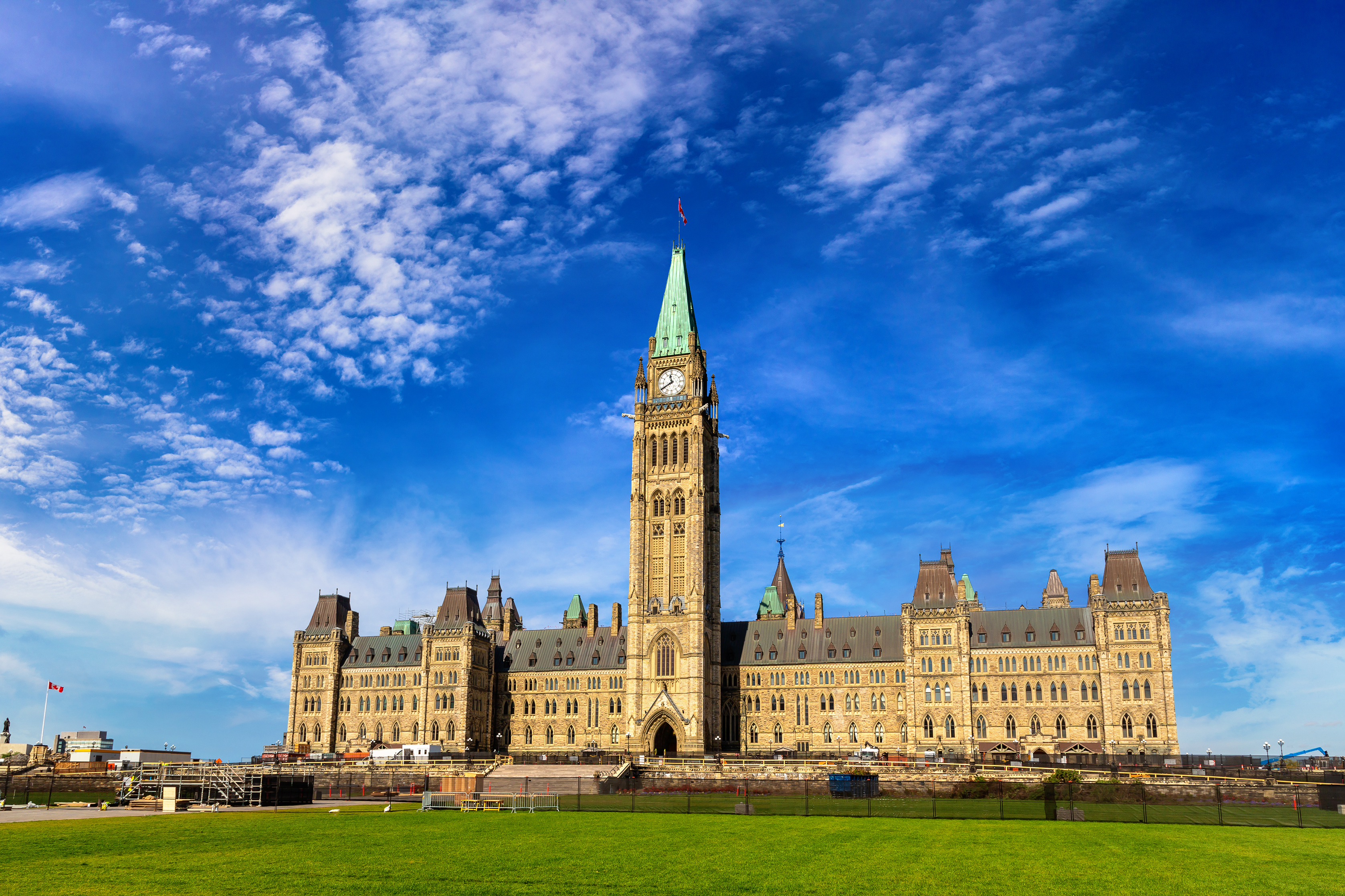 Les bâtiments du Parlement canadien à Ottawa, sous un ciel d'un bleu éclatant parsemé de quelques nuages, vus depuis la pelouse devant le Parlement.