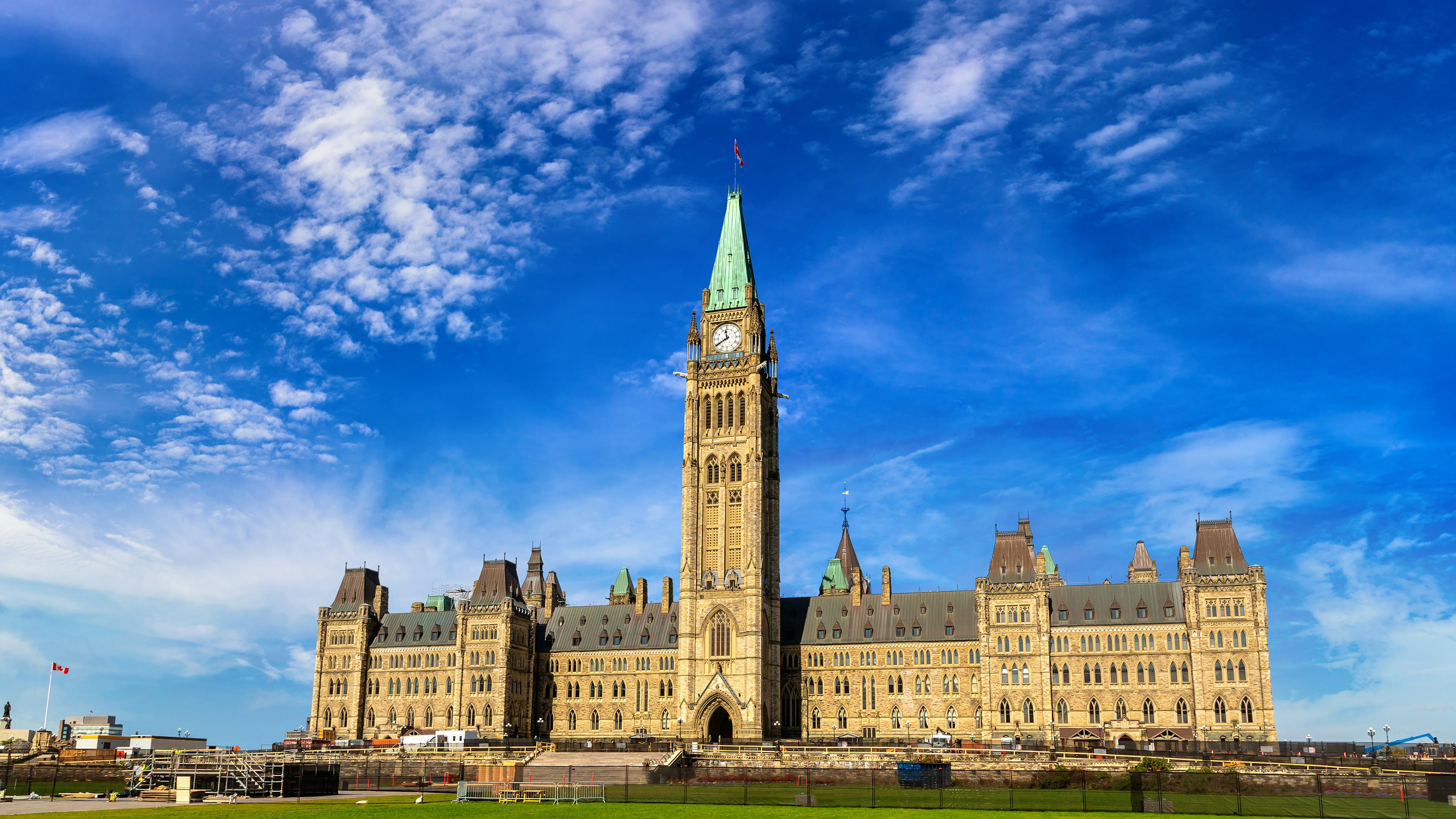Les bâtiments du Parlement canadien à Ottawa, sous un ciel d'un bleu éclatant parsemé de quelques nuages, vus depuis la pelouse devant le Parlement.