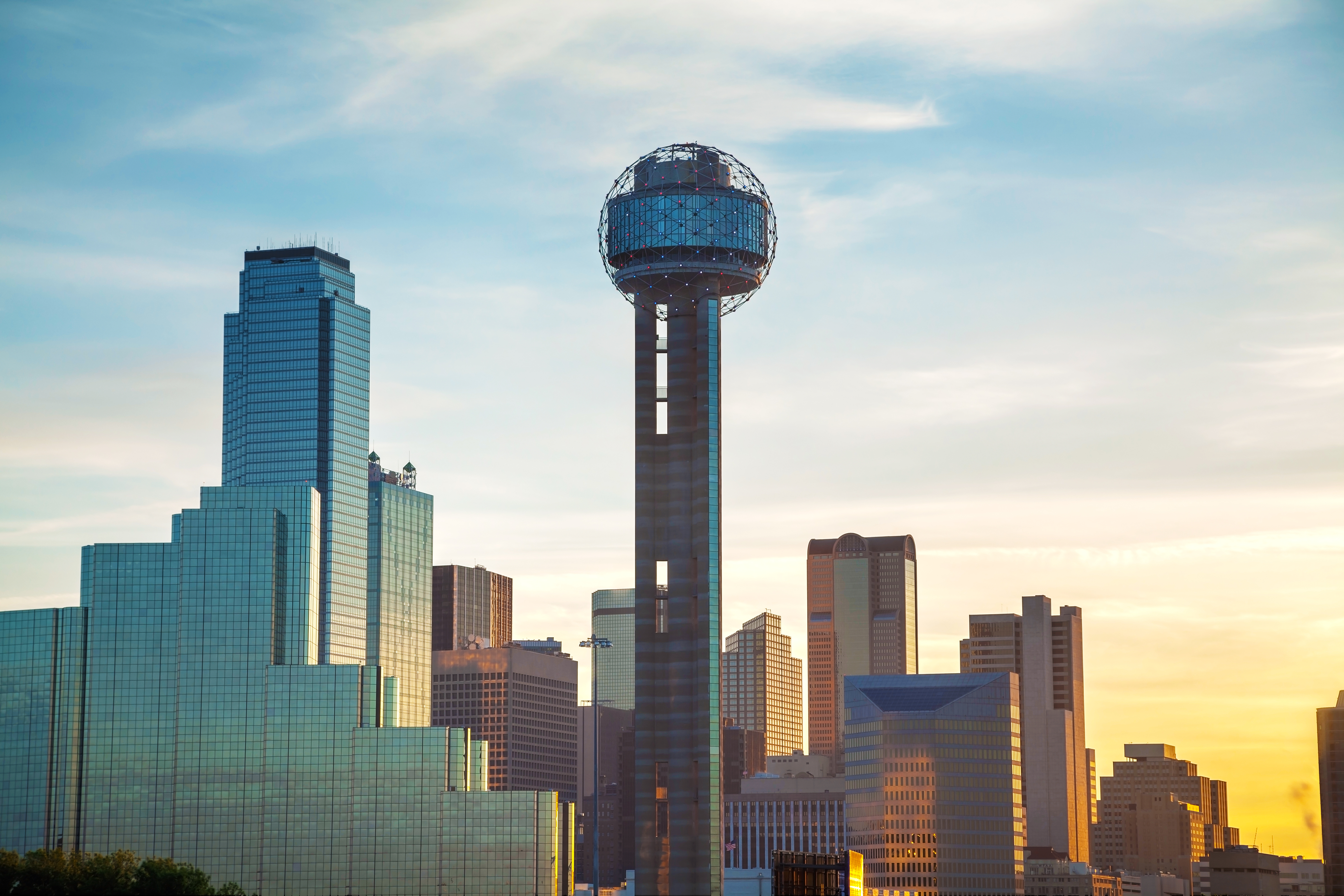 La ligne d'horizon de Dallas au coucher du soleil, avec la Reunion Tower, un imposant édifice surmonté d'un dôme géodésique, qui se détache nettement parmi les gratte-ciel modernes, sur fond de ciel coloré.