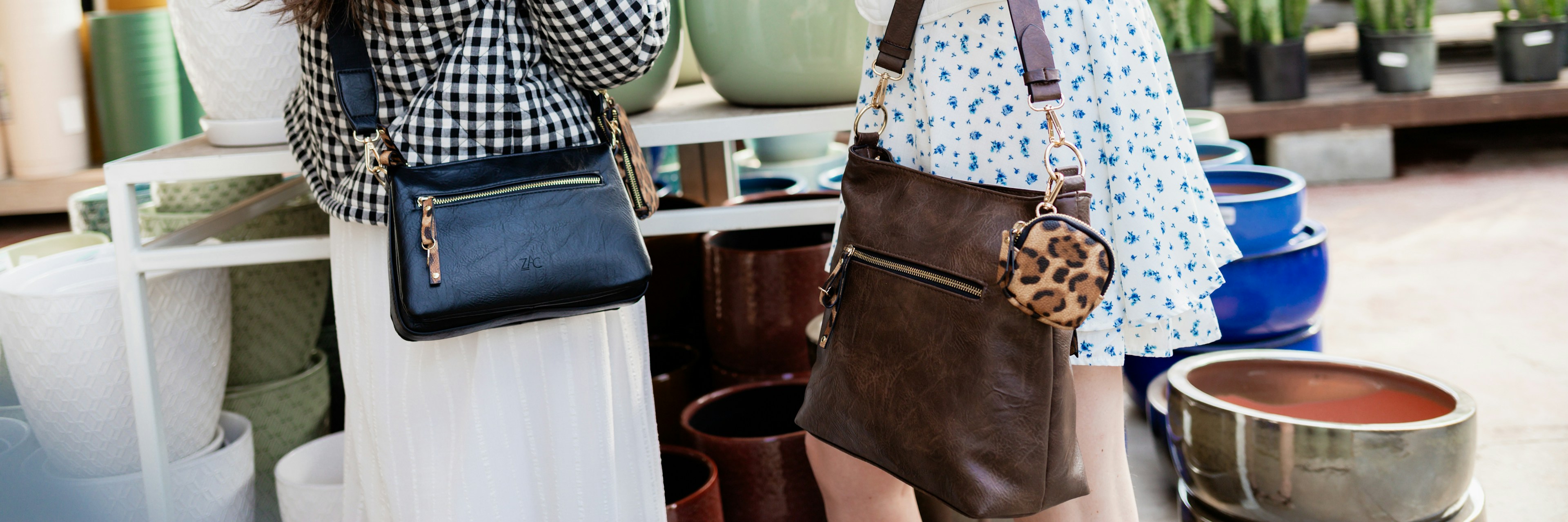 Deux femmes se tiennent dans une jardinerie, souriantes, un sac en bandoulière à la main. En arrière-plan, des étagères regorgent de pots en céramique et de plantes vertes feuillues. L'une porte une veste à carreaux, l'autre une veste blanche ornée d'écussons en forme d'étoile.