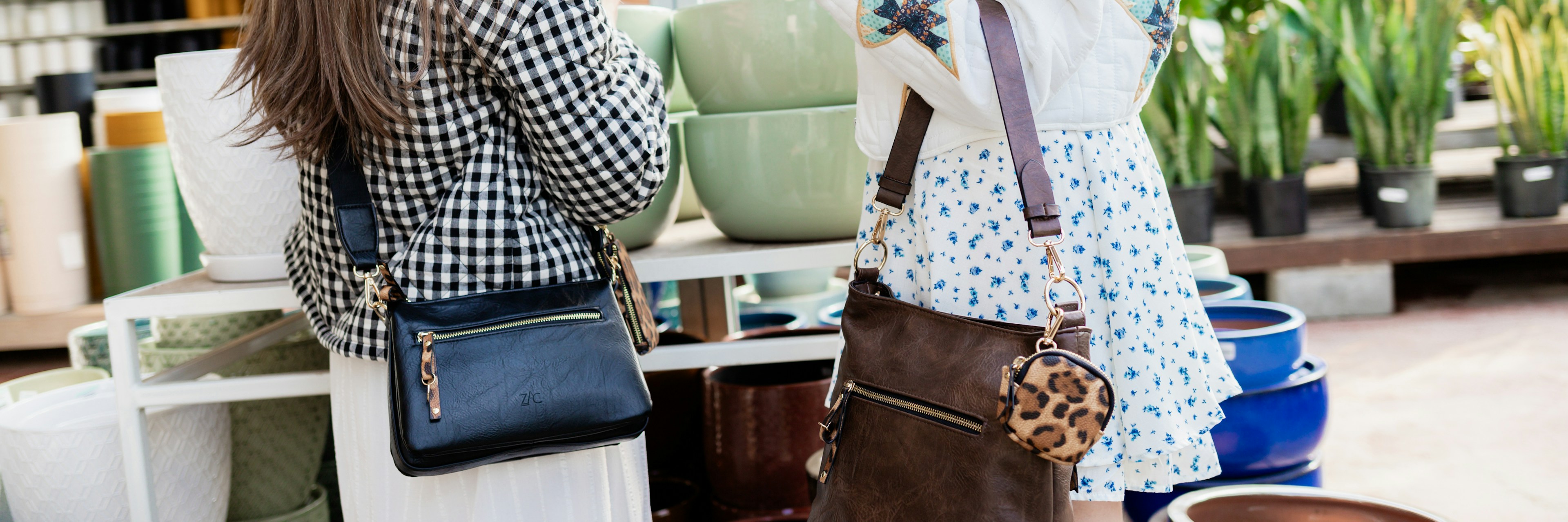 Two women stand in a plant shop, each carrying handbags. One wears a checkered jacket, the other a white jacket with star patches. Colorful pots and green plants are visible in the background.